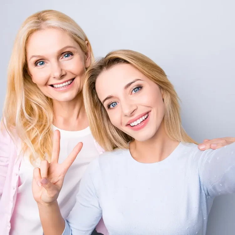 two ladies wearing white and smiling happily together while holding up peace sign taking selfie
