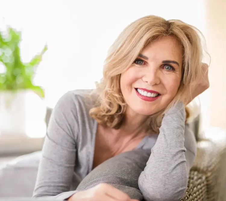 older lady wearing grey dress and sitting on couch while smiling with beautiful white teeth