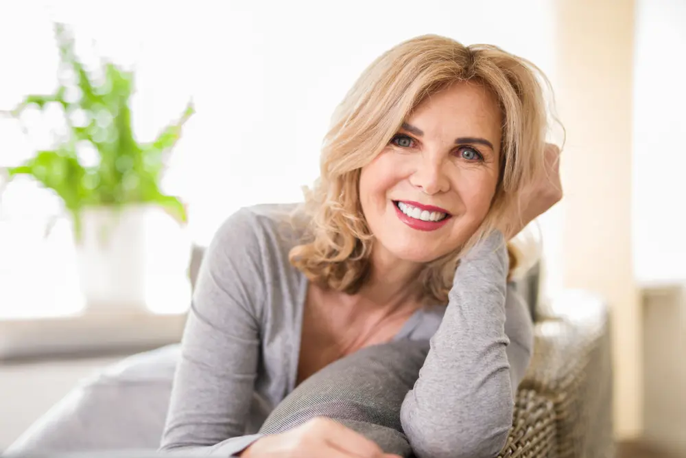 older lady wearing grey dress and sitting on couch while smiling with beautiful white teeth