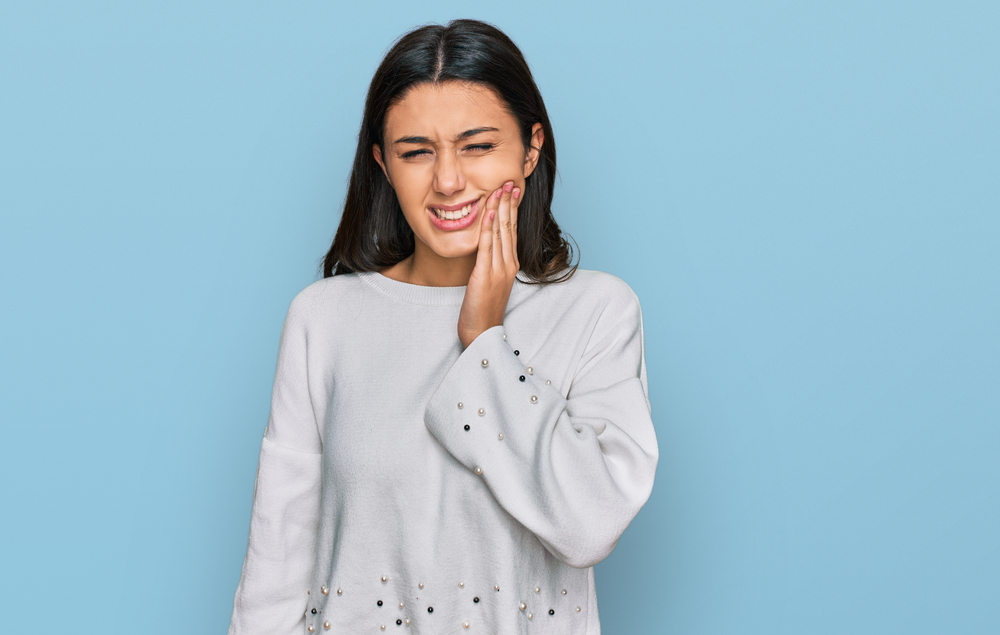 young hispanic girl wearing a sweater touching the side of her face while in pain Emergency Dentistry Duncan